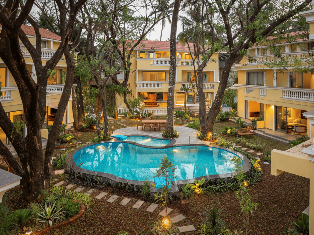 Cluster of traditional Goan-style villas with central pool, trees, side seating, and lawn with walking path