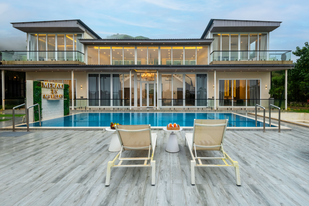 Duplex villa with modern structure, glass windows, private pool, relaxing chairs, fruit table, and serene Lonavala hill views
